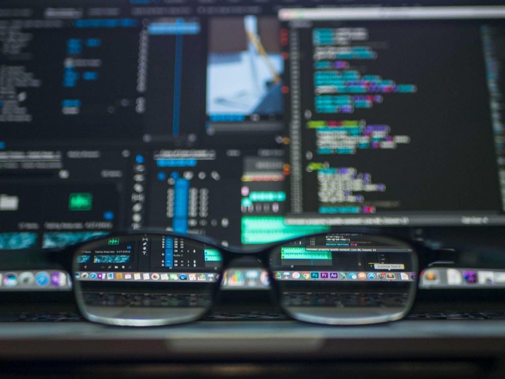 A pair of glasses sit in front of a computer monitor with code, representing ThriveDX’s cybersecurity bootcamps